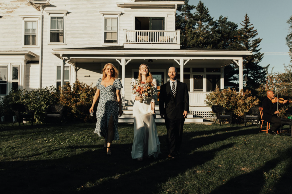 A bride walks down the aisle with her mother and father as a wedding string quartet plays.